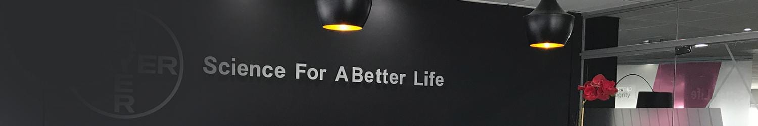 Interior de una oficina con una pared negra que muestra el texto "Ciencia para una vida mejor" en blanco. Las luces colgantes iluminan el área y se ve una flor roja a la derecha.