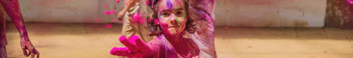 Un niño con polvos de colores en la cara y la mano se extiende hacia adelante durante la celebración de un festival.