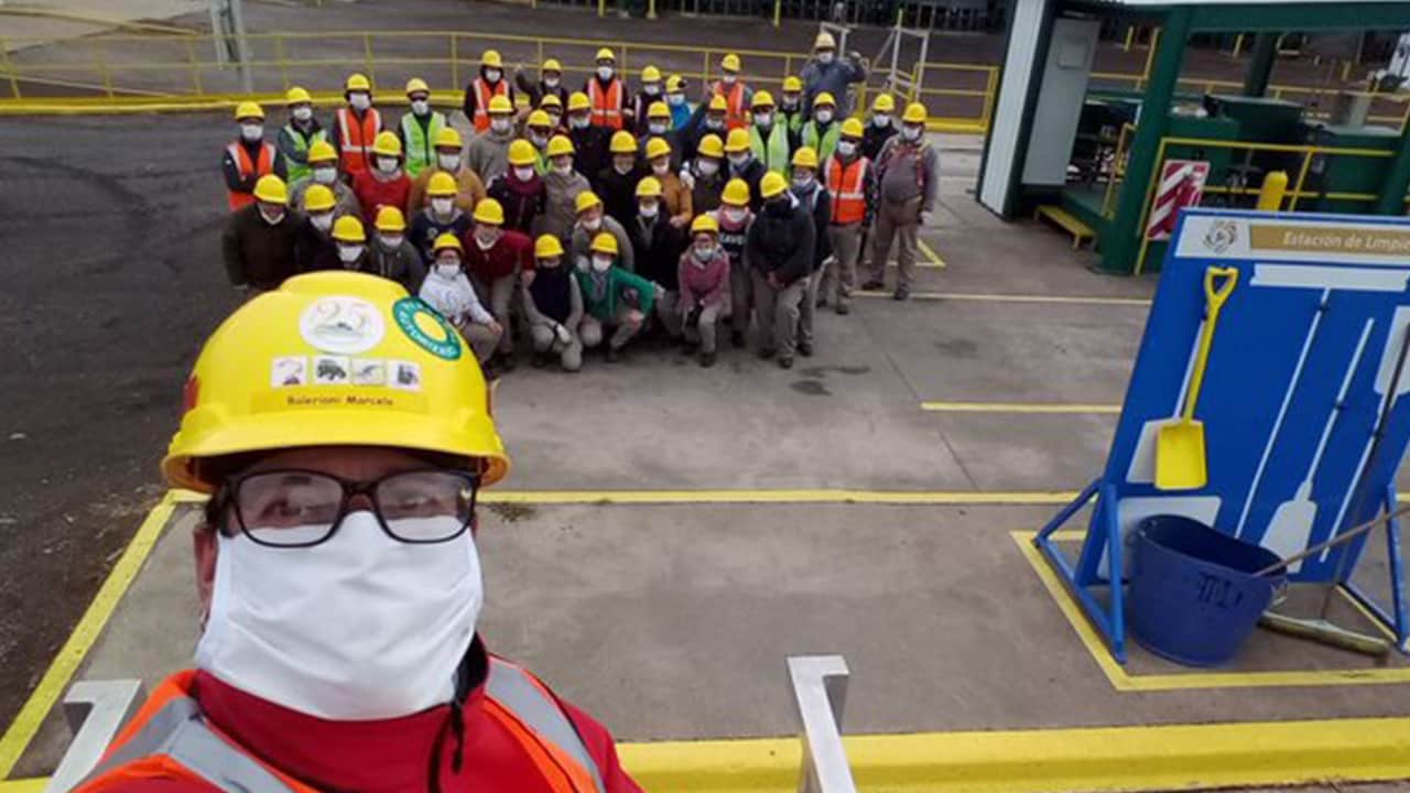Un grupo de trabajadores de la construcción con equipo de seguridad y cascos posa para una foto grupal en una obra. Una persona en primer plano se toma el selfie.