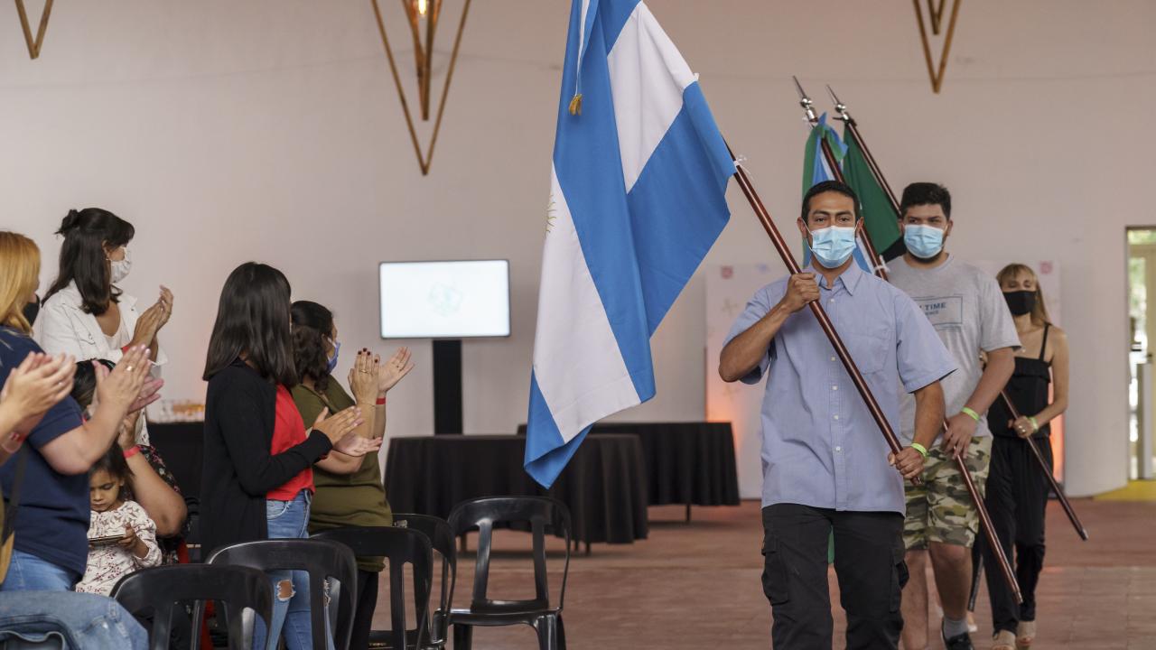 La gente en una sala aplaude mientras una persona pasa portando una bandera.