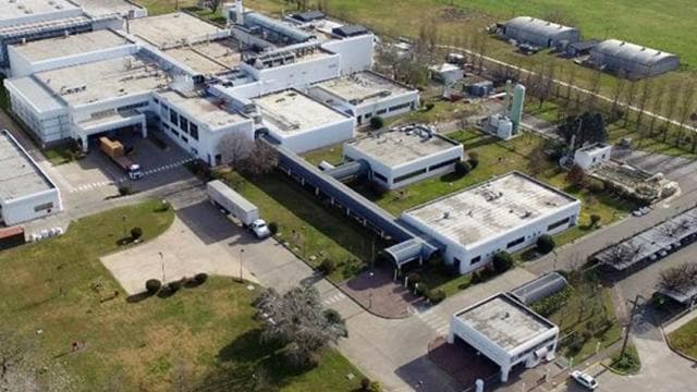 Vista aérea de una instalación industrial con varios edificios blancos, camiones y vegetación circundante.