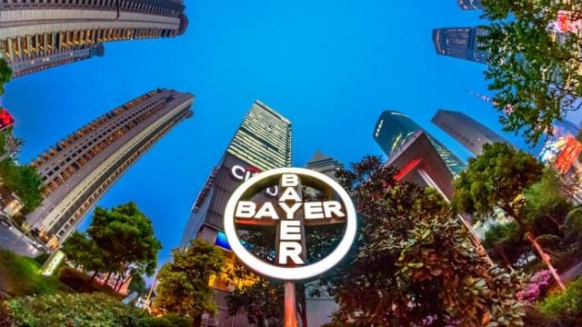 Vista de ojo de pez de un paisaje urbano con edificios altos y un destacado cartel de Bayer en primer plano.
