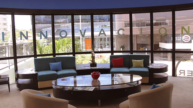 Moderno salón de oficina con asientos circulares, mesa de cristal y grandes ventanales que muestran la palabra "INNOVACION".