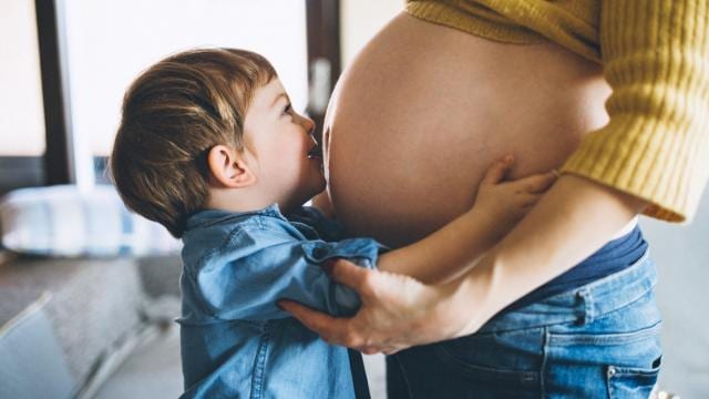Un niño pequeño abraza y besa el vientre de una persona embarazada en una sala de estar.