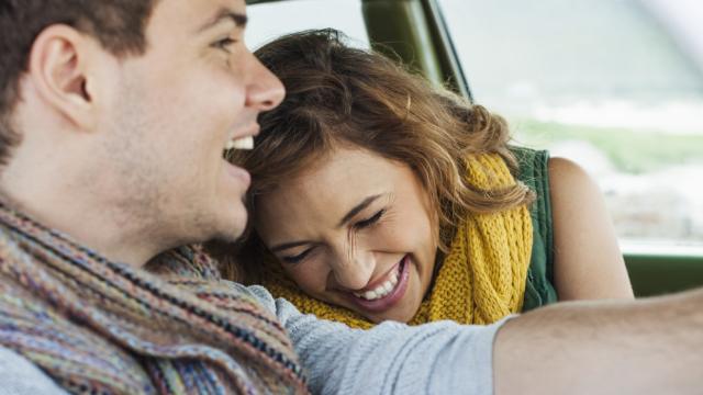 Un hombre y una mujer sonrientes, ambos con bufandas, están sentados juntos en un automóvil.