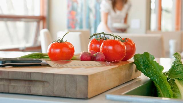 Las verduras frescas, incluidos tomates, rábanos y lechuga, se colocan en una tabla de cortar de madera con un cuchillo.