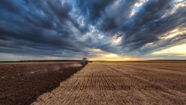 Un tractor ara un campo bajo un espectacular cielo nublado al atardecer, dividiendo una sección cultivada de otra cosechada.