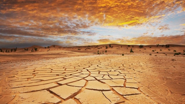 Paisaje desértico agrietado y seco bajo un espectacular cielo de atardecer con nubes dispersas y dunas distantes.