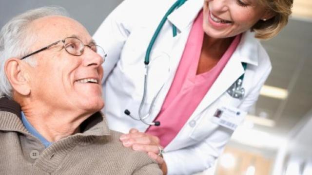 Un hombre mayor sonríe mientras una médica con bata blanca le habla, colocándole una mano sobre el hombro.