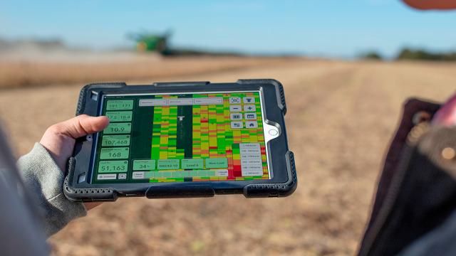 Dos personas en un campo miran una tableta que muestra datos agrícolas y mapas.