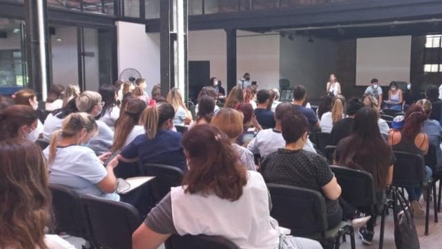 Un grupo de personas sentadas en sillas asistiendo a una presentación o reunión en interiores.