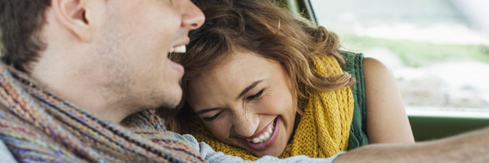 Un hombre y una mujer sonrientes, ambos con bufandas, están sentados juntos en un automóvil.
