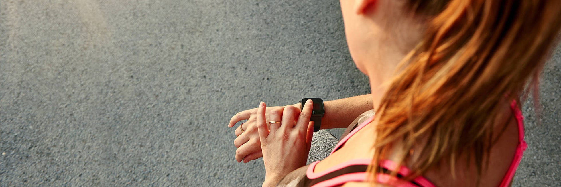 Una mujer vestida con ropa deportiva mira su reloj inteligente mientras está parada en una calle pavimentada.