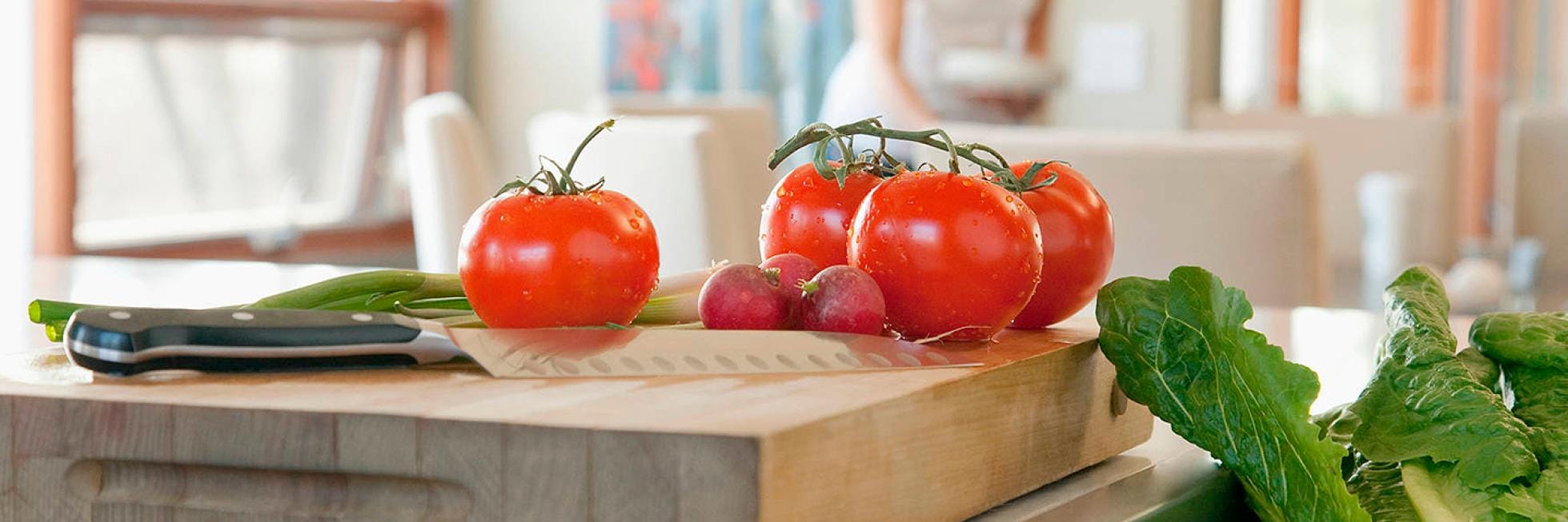 Las verduras frescas, incluidos tomates, rábanos y lechuga, se colocan en una tabla de cortar de madera con un cuchillo.