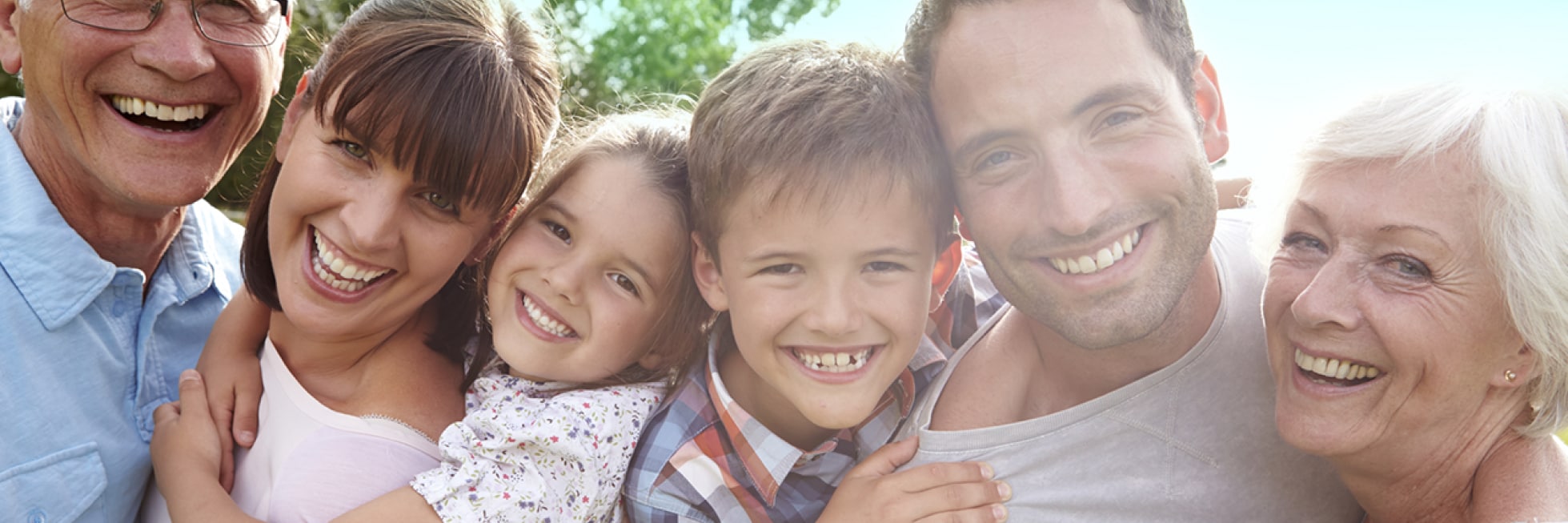 Una familia feliz de seis personas, incluidos tres adultos, dos niños y un adulto mayor, sonríe al aire libre en un día soleado.