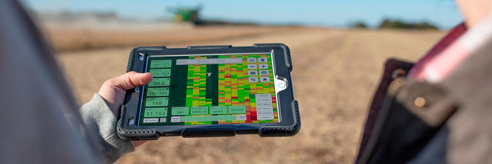 Dos personas en un campo miran una tableta que muestra datos agrícolas y mapas.