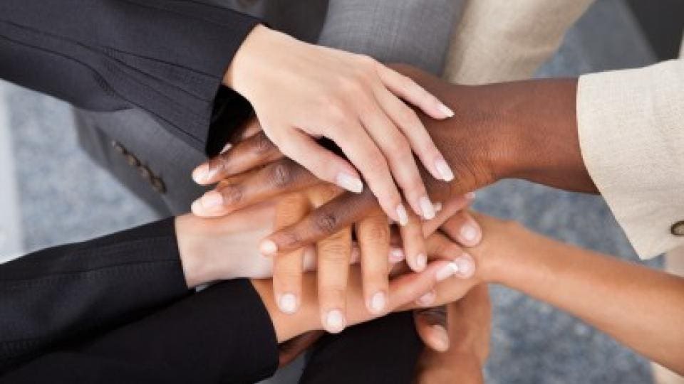 Un grupo de manos diversas unidas en el centro, simbolizando la unidad y el trabajo en equipo.
