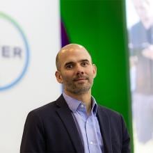 Una persona con traje se encuentra frente a un cartel de Bayer.